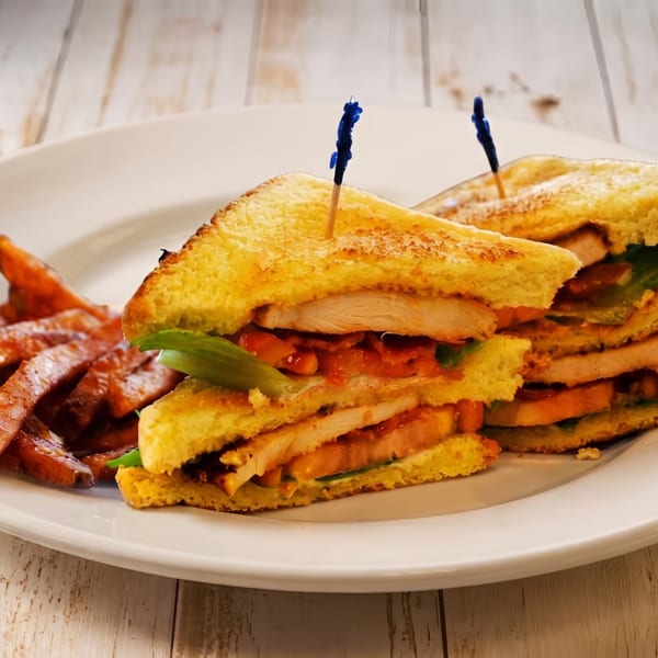 Two toasted chicken club sandwiches with lettuce and sweet potato fries on a white plate.