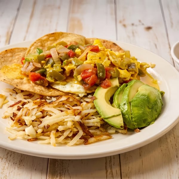 Scrambled eggs and vegetables on tortillas, hash browns, avocado, and salsa on a white plate.